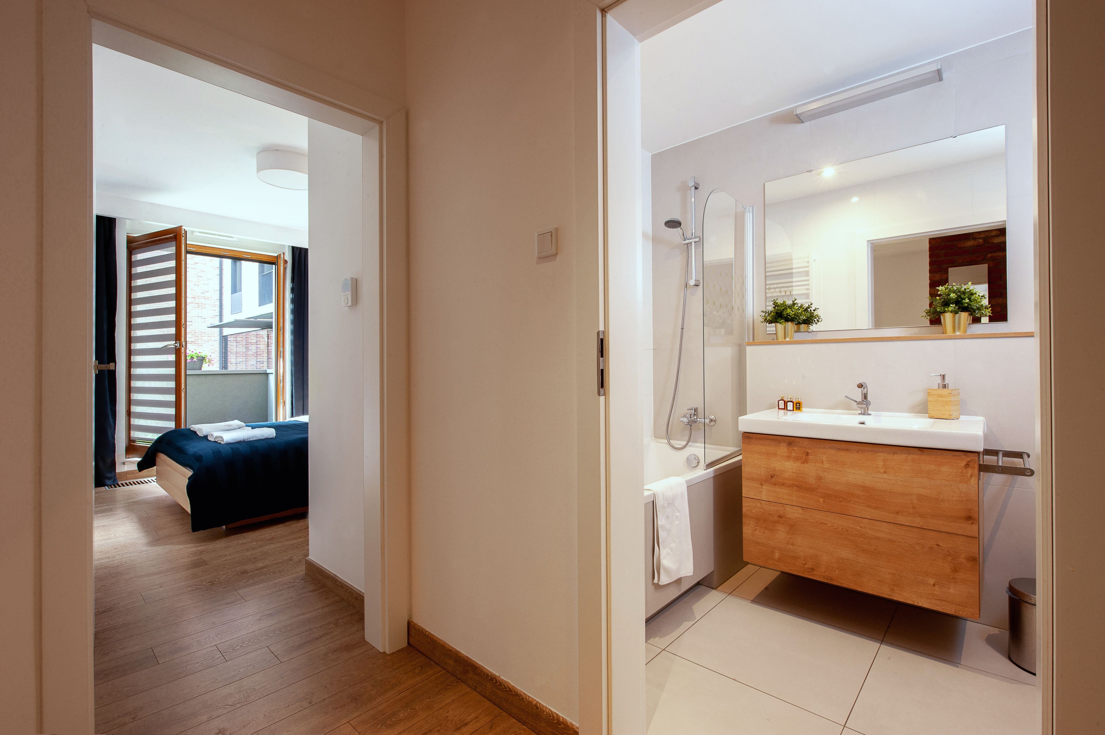Une salle de bain moderne avec une douche, un lavabo et un miroir. On y trouve un meuble en bois sous le lavabo et une serviette accrochée au mur.