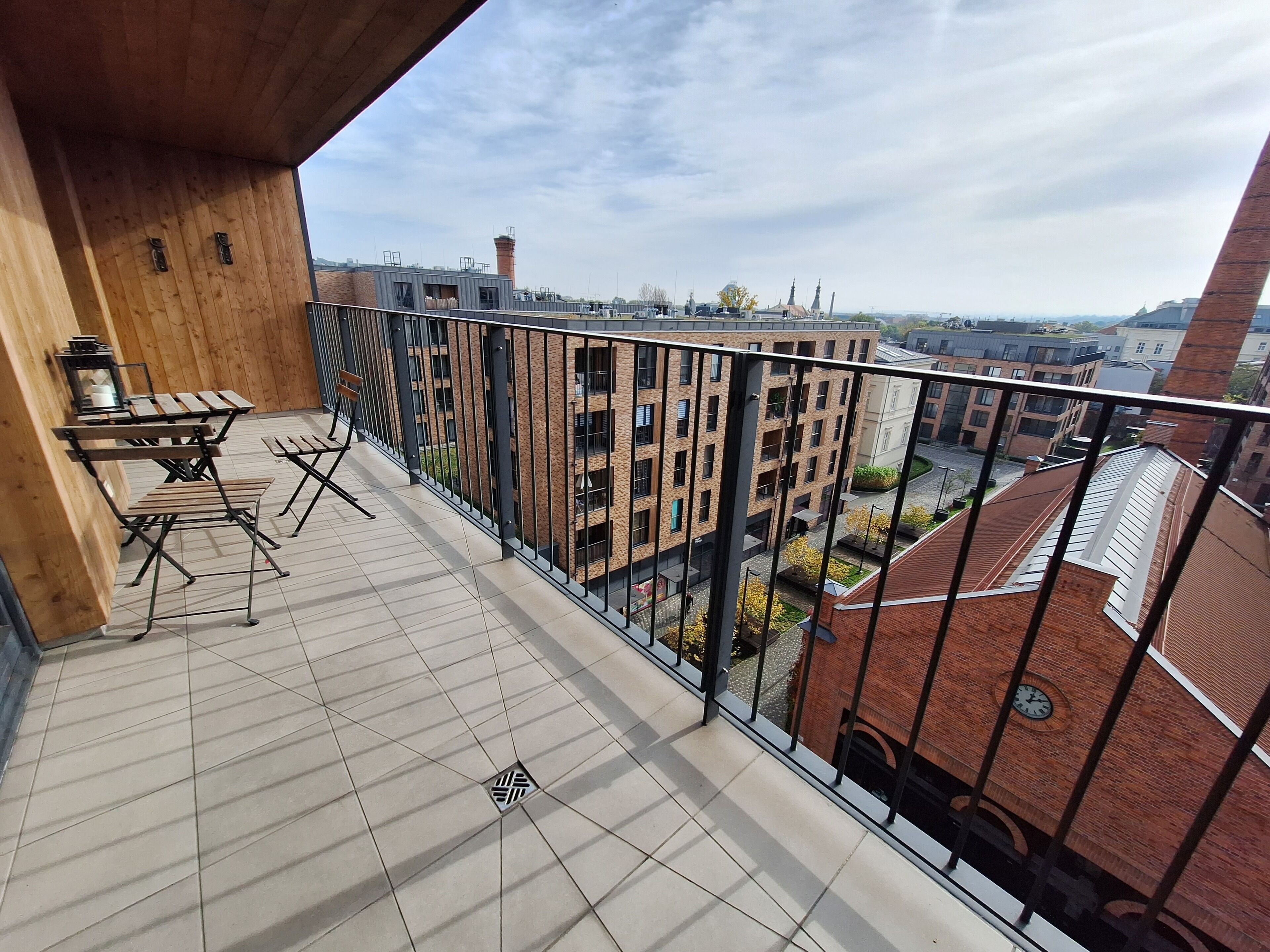 A balcony with a wooden table and chairs, a tiled floor, and a view of surrounding buildings.
