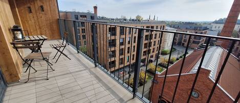 A balcony with a wooden table and chairs, a tiled floor, and a view of surrounding buildings.