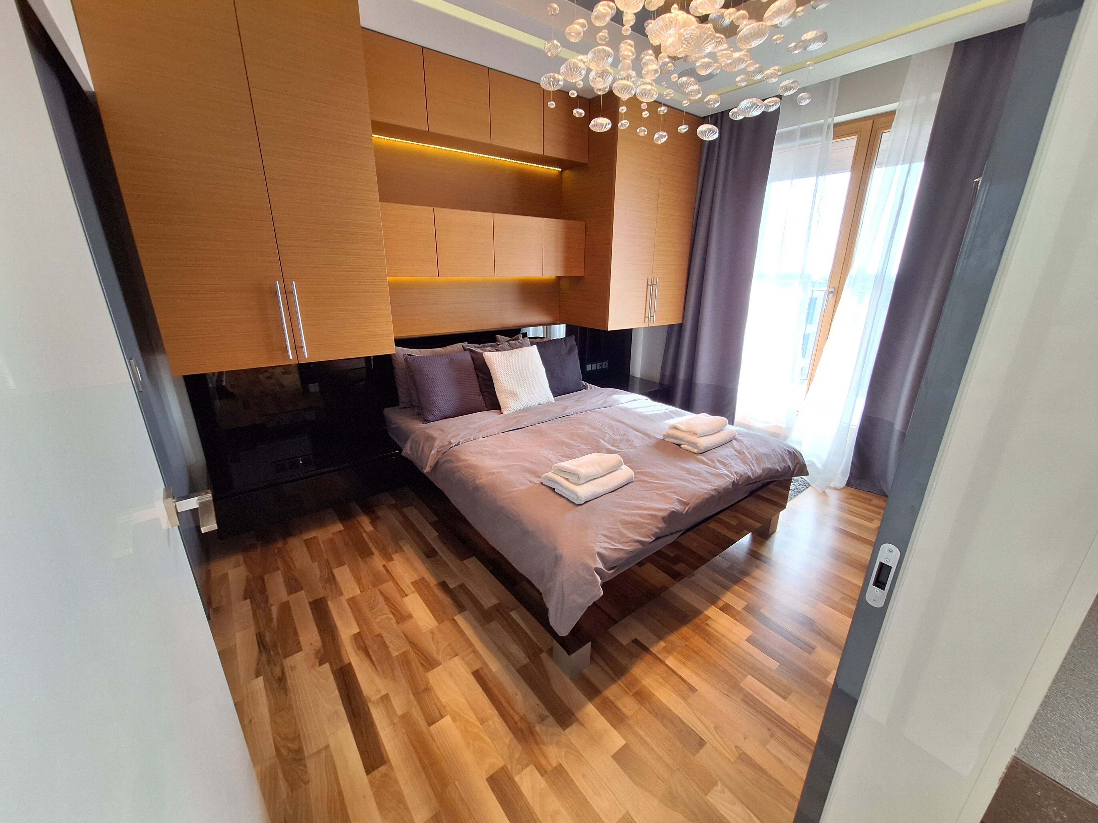 Um quarto moderno com piso de madeira, uma cama com encosto e um luminário de teto.