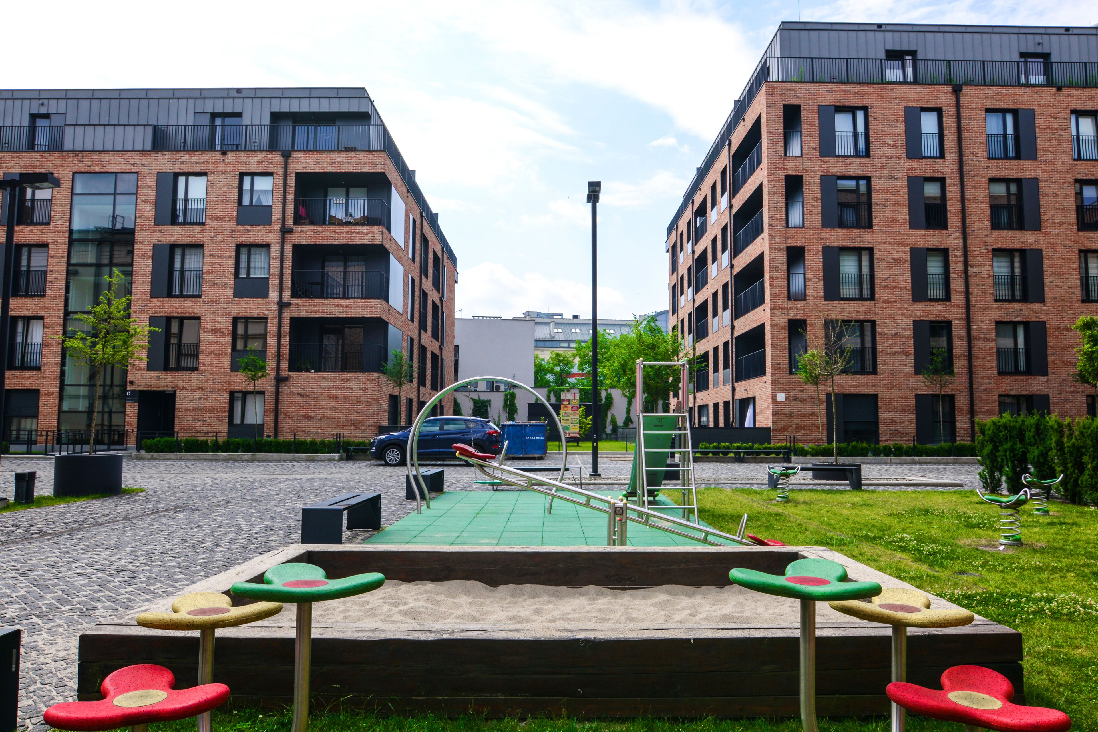 A playground with swings and a seesaw in front of a brick building with multiple windows.