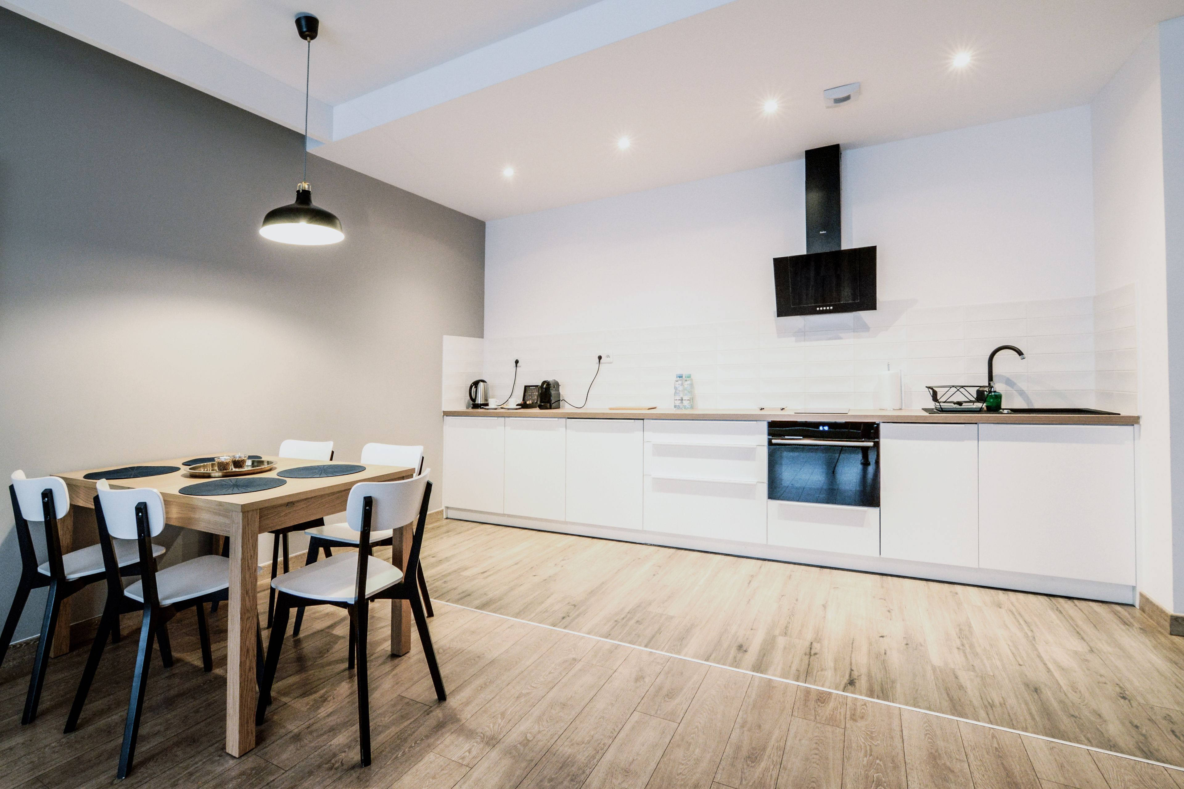 A modern kitchen with white cabinets, a wooden dining table, and a black pendant light.