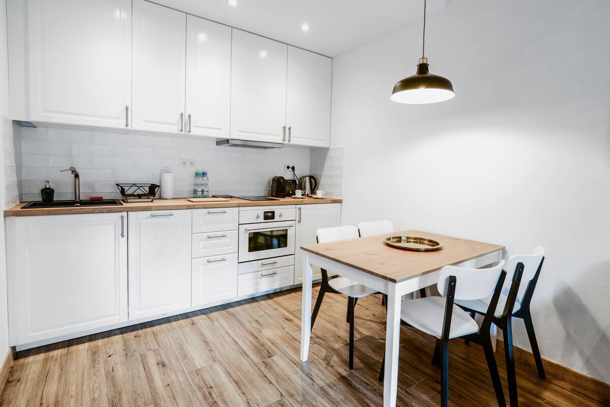 Una cocina moderna con armarios blancos, encimera de madera, una mesa de comedor con sillas y una lámpara colgante.