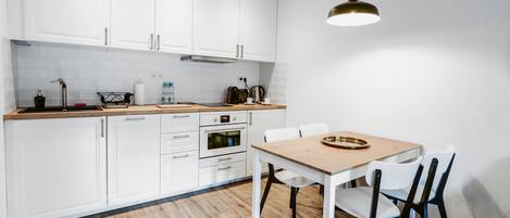 Une cuisine moderne avec des armoires blanches, un plan de travail en bois, une table à manger avec des chaises et un luminaire suspendu.