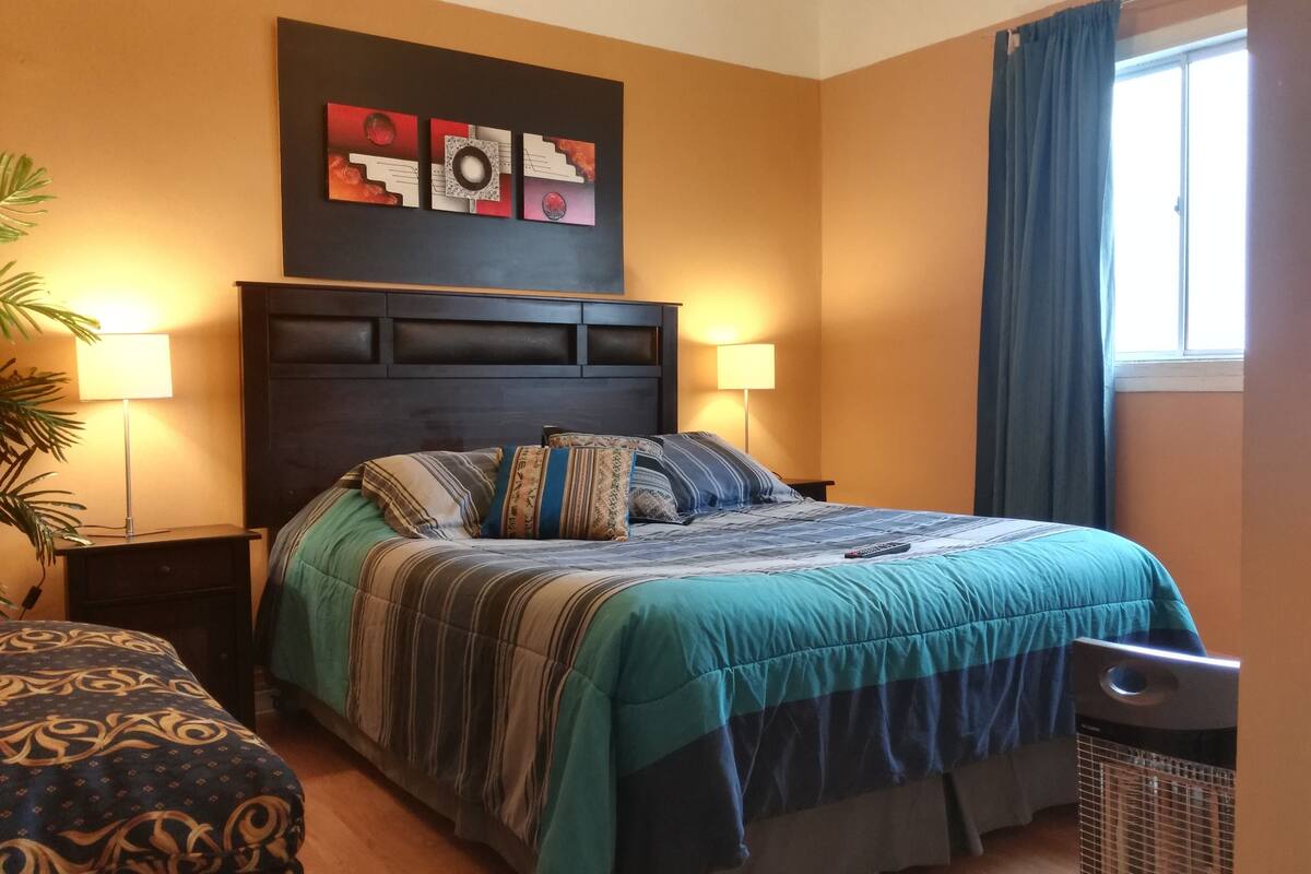 A bedroom with a bed, two bedside lamps, a wall art piece, and a window with curtains.
