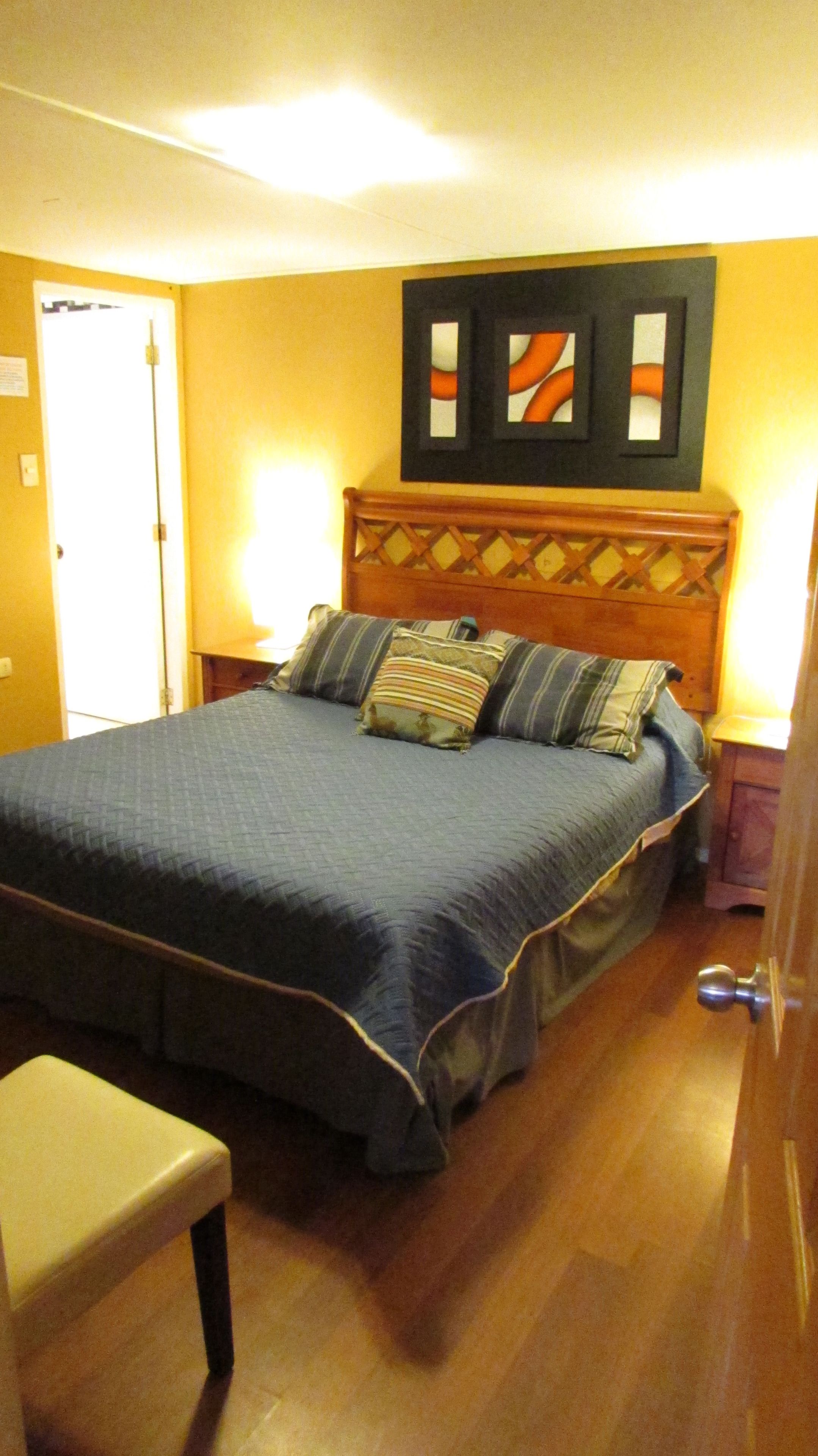 Quarto com cama, um banco, cabeceira de madeira e uma porta.