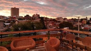 Een balkon met rieten meubels en een uitzicht op een stadsgezicht bij zonsondergang.