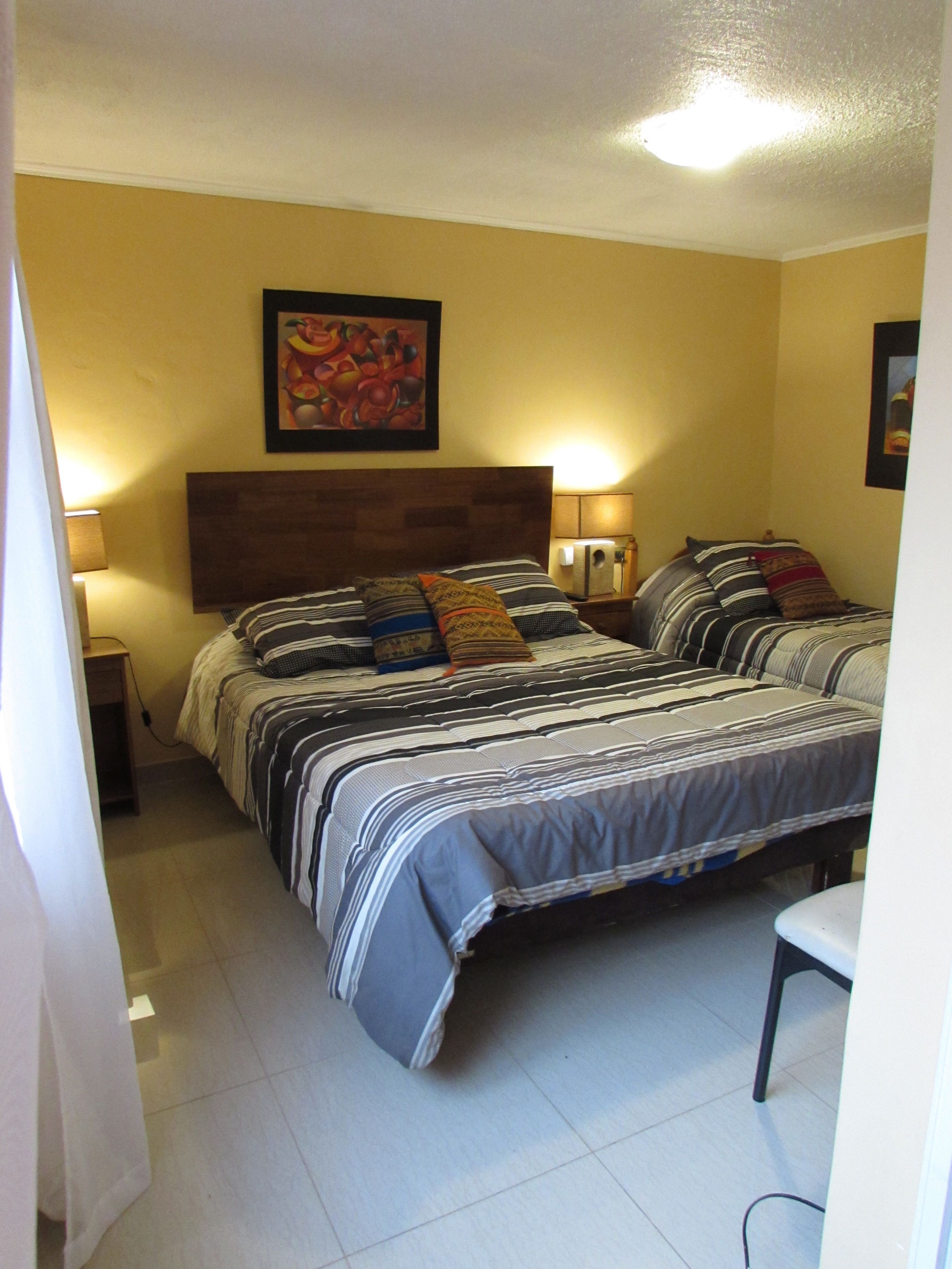Uma cama de casal com roupa de cama listrada, uma cabeceira de madeira e duas luminárias de apoio.