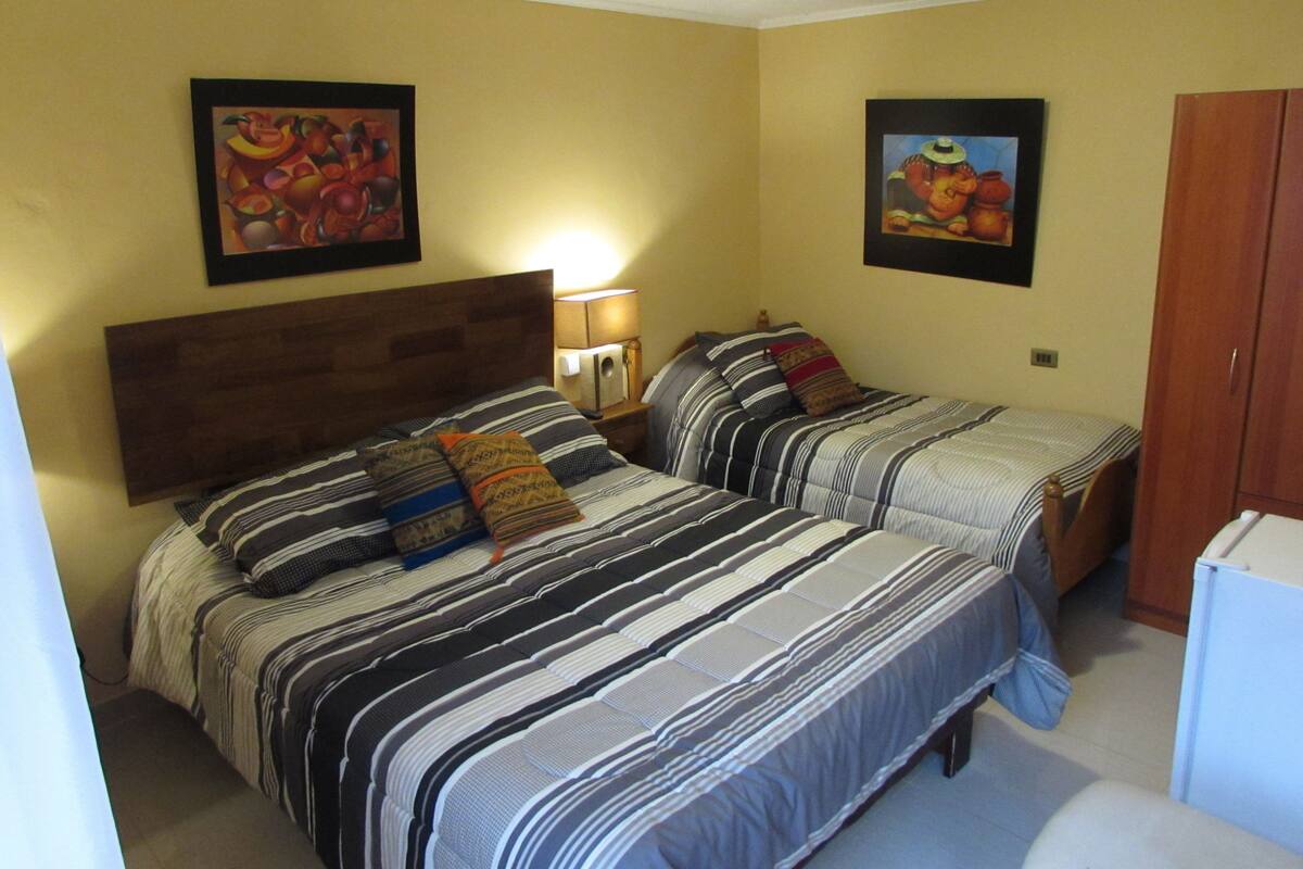 A bedroom with two beds, a wooden headboard, a nightstand with a lamp, and two framed pictures on the wall.