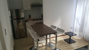 A compact kitchen with a refrigerator, stove, and white chairs. - Room Plaza Cousino (Santiago)