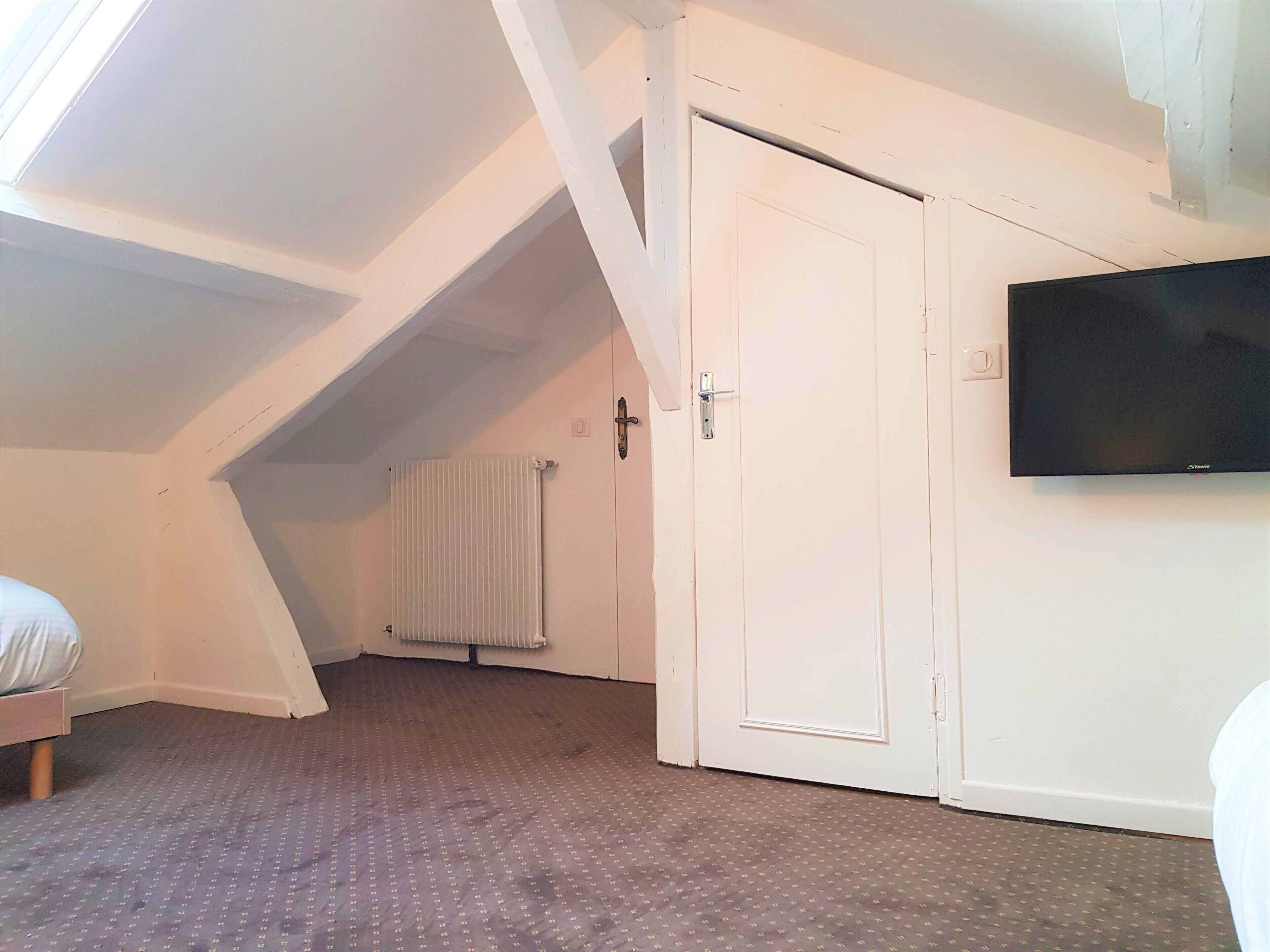 A room with a sloped ceiling, a radiator, a white door, and a mounted television.