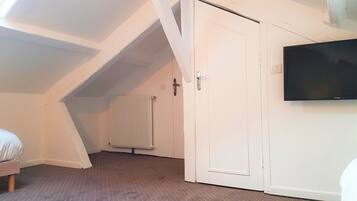 A room with a sloped ceiling, a radiator, a white door, and a mounted television.