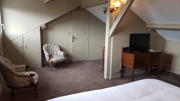 Een slaapkamer met een groot bed, een stoel, een bureau met een televisie en een kledingkast.