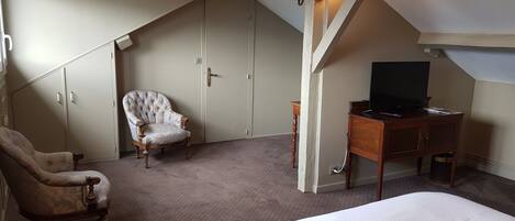 A bedroom with a large bed, a chair, a desk with a TV, and a wardrobe.