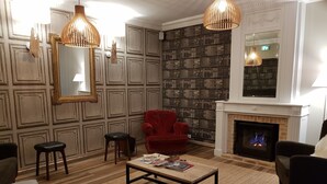 A room with a fireplace, a red armchair, a coffee table with magazines, and a bookshelf. - Les Cabines (Houlgate)