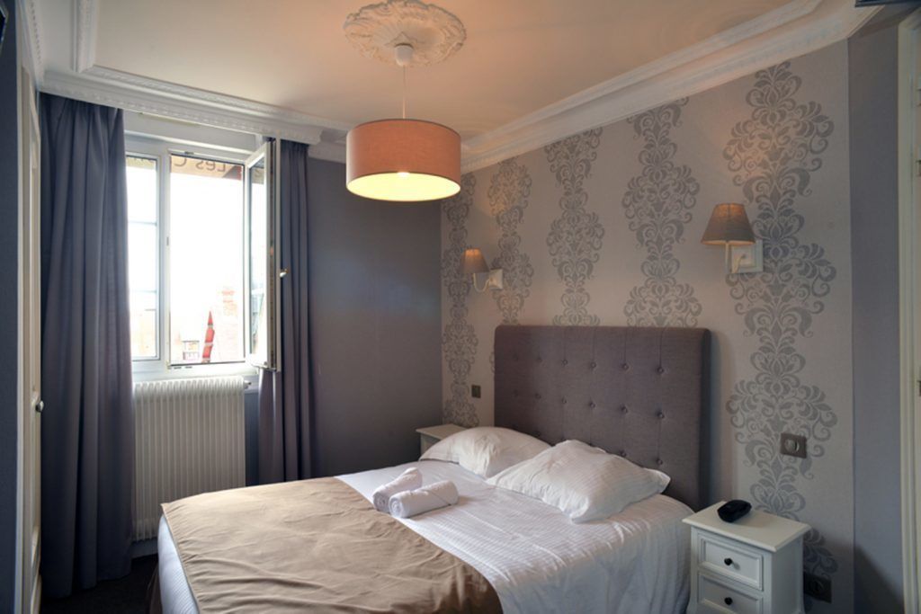 A neatly arranged bedroom with a large bed, a bedside table, and a window with curtains.