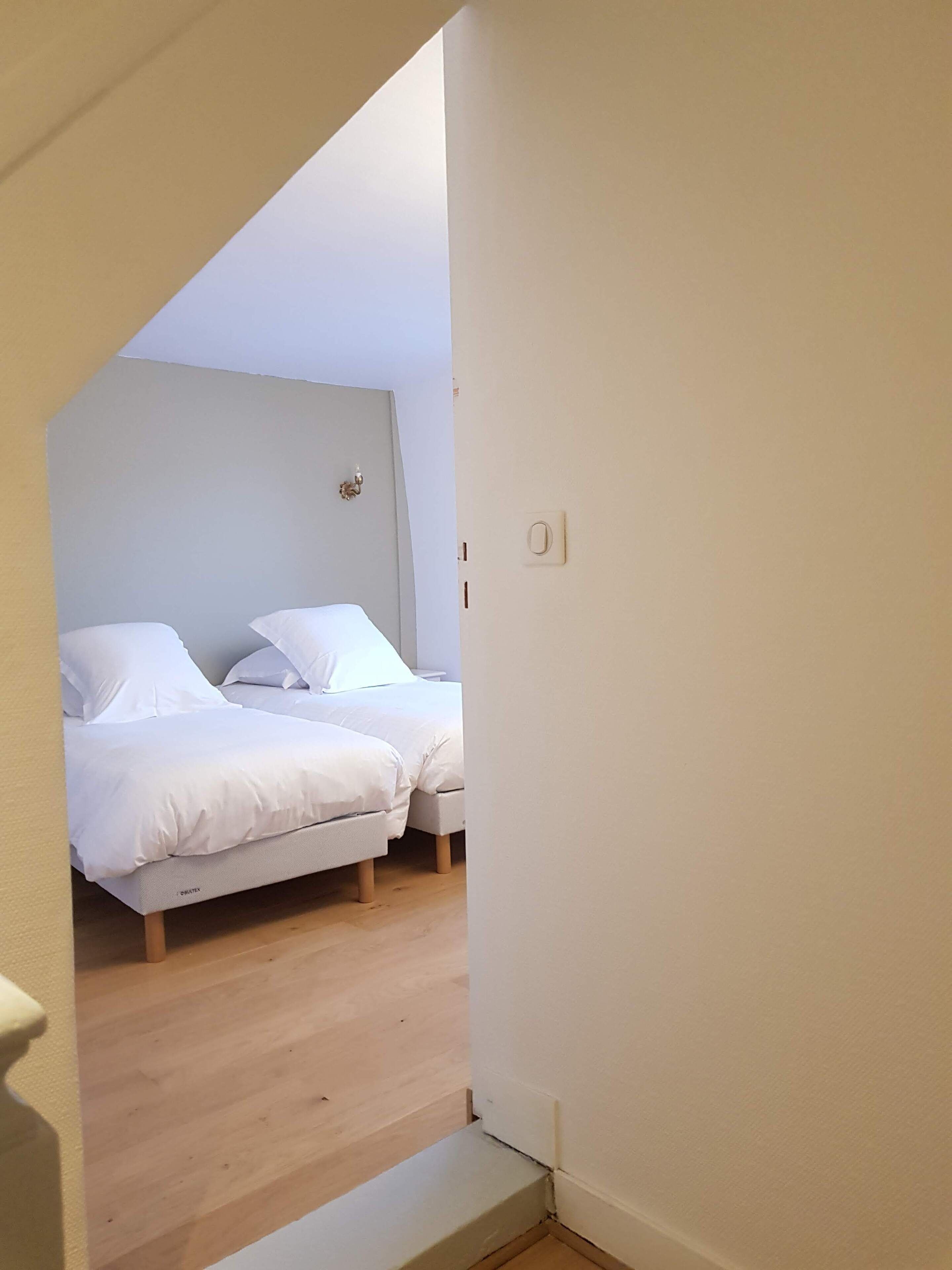 A bedroom with two beds, wooden flooring, and a light-colored wall.