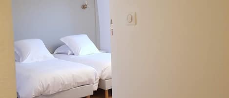 A bedroom with two beds, wooden flooring, and a light-colored wall.