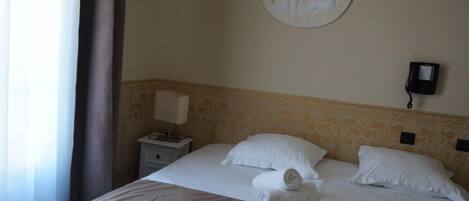 A hotel room with a bed, a bedside table with a lamp, a telephone, and a wall-mounted artwork.