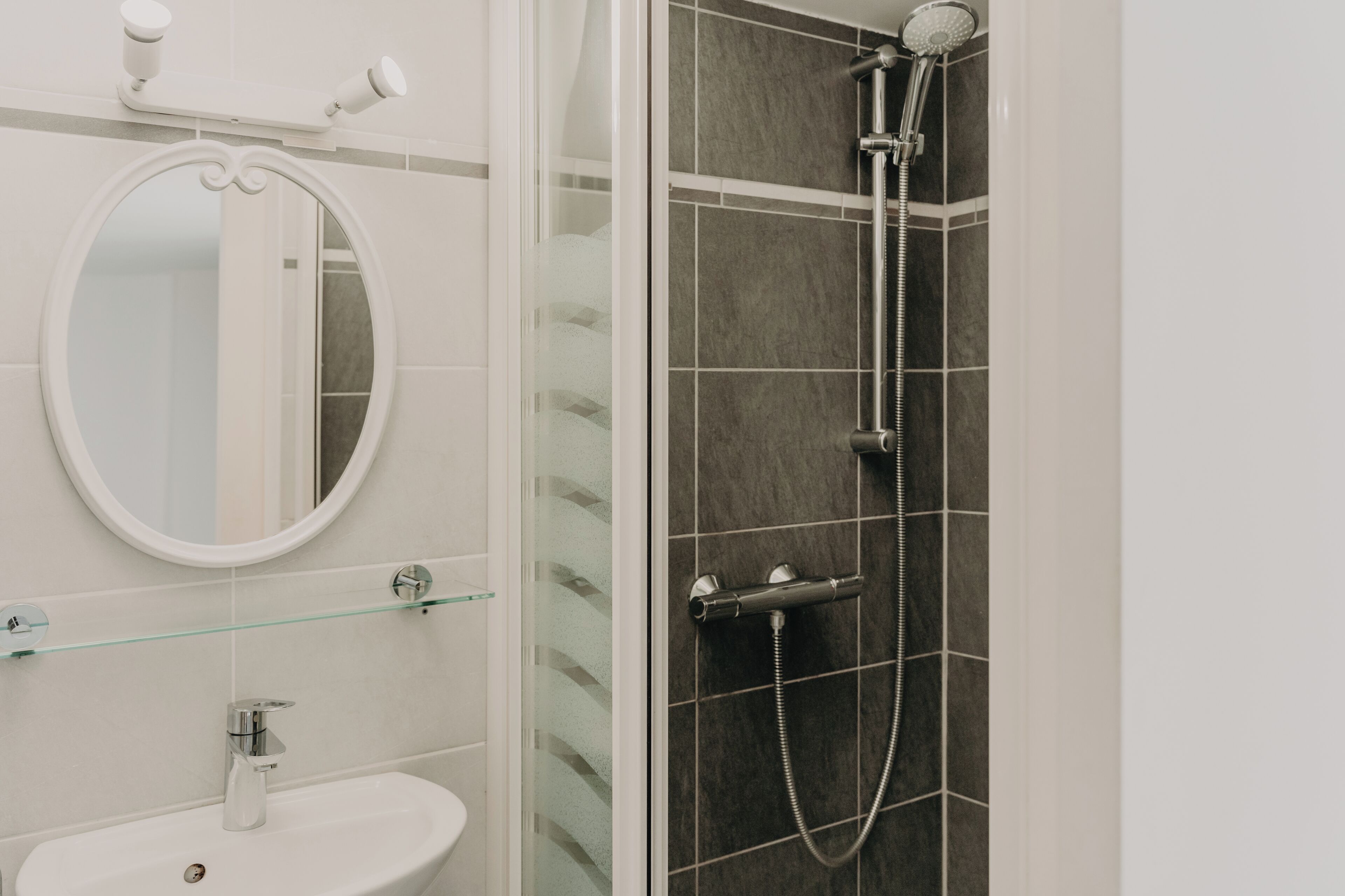 A bathroom with a white sink, a round mirror, and a shower with a handheld showerhead.