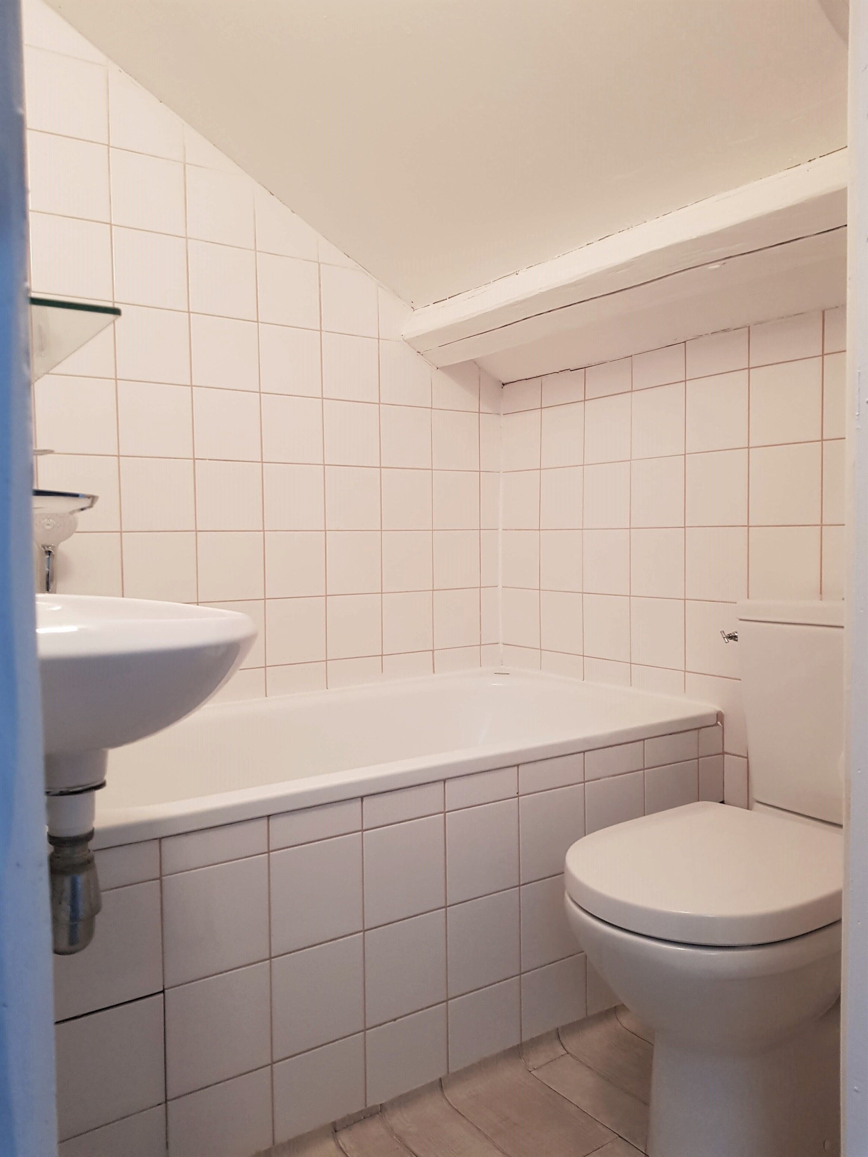 Un baño con azulejos blancos, una bañera blanca y un inodoro blanco.