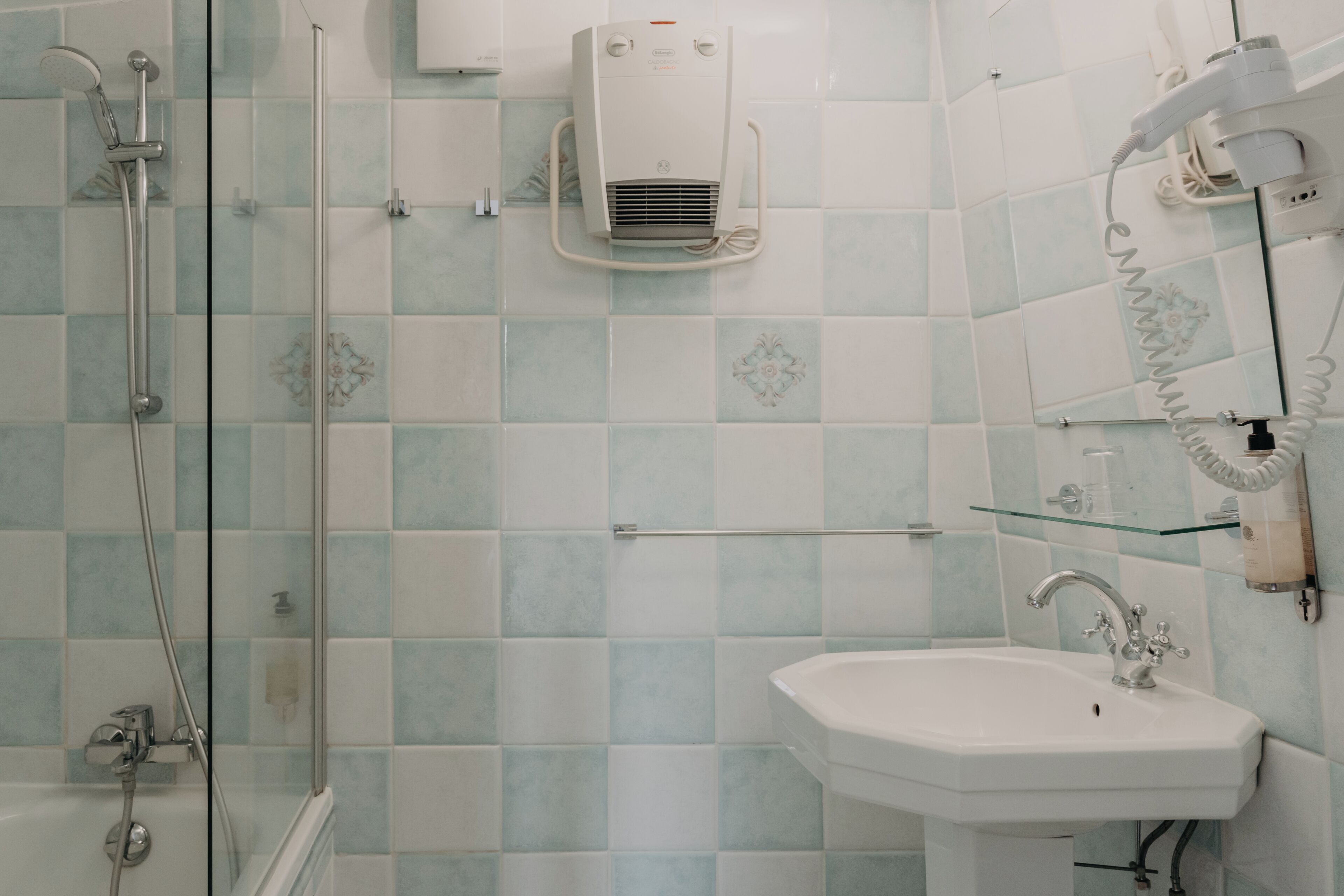 Un baño con cabina de ducha de vidrio, un lavabo blanco y un aire acondicionado de pared.