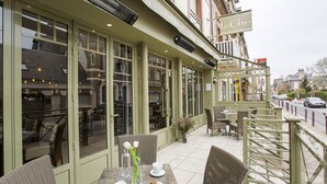 An outdoor cafe with tables and chairs, a flower vase, and a sign for "Les Cabines." - Les Cabines (Houlgate)