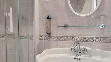 Un baño con cabina de ducha de vidrio, un lavamanos sobre pedestal y un espejo encima, además de un estante de vidrio.