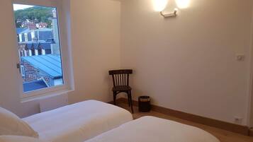 A bedroom with two beds, a window, a chair, and a wall-mounted light fixture.