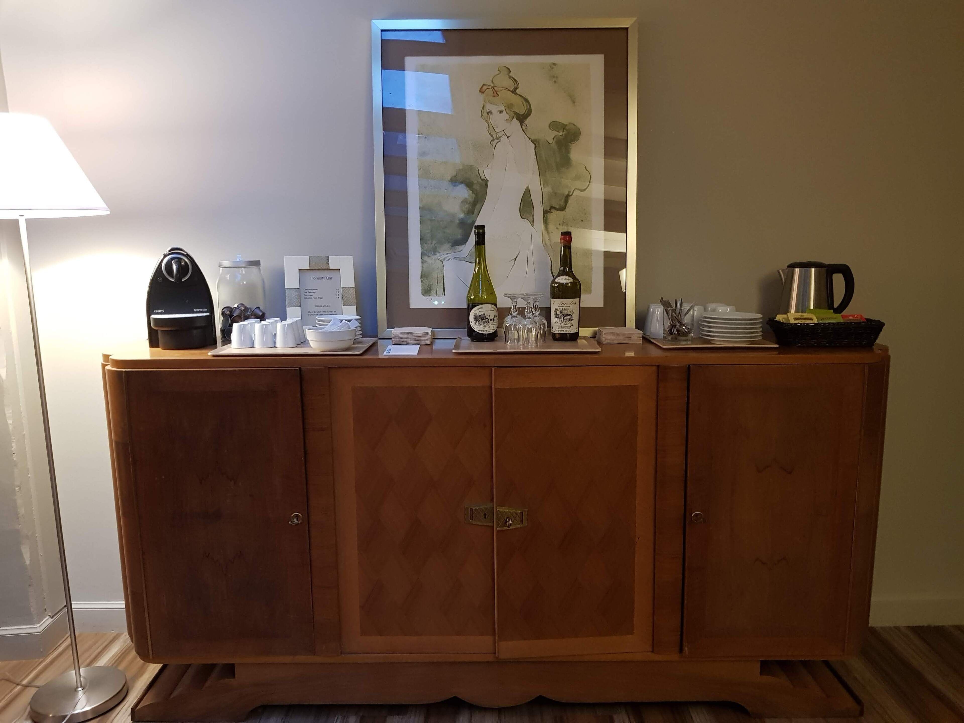 Un mostrador de recepción de madera con una obra de arte enmarcada encima, una cafetera y una jarra de café a la izquierda.