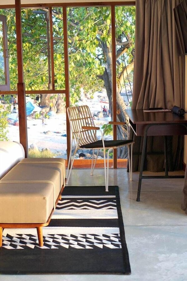 A room with a bed, a chair, a table, and a view of a beach. - Tamarina Bed and Beyond (Koh Samui)