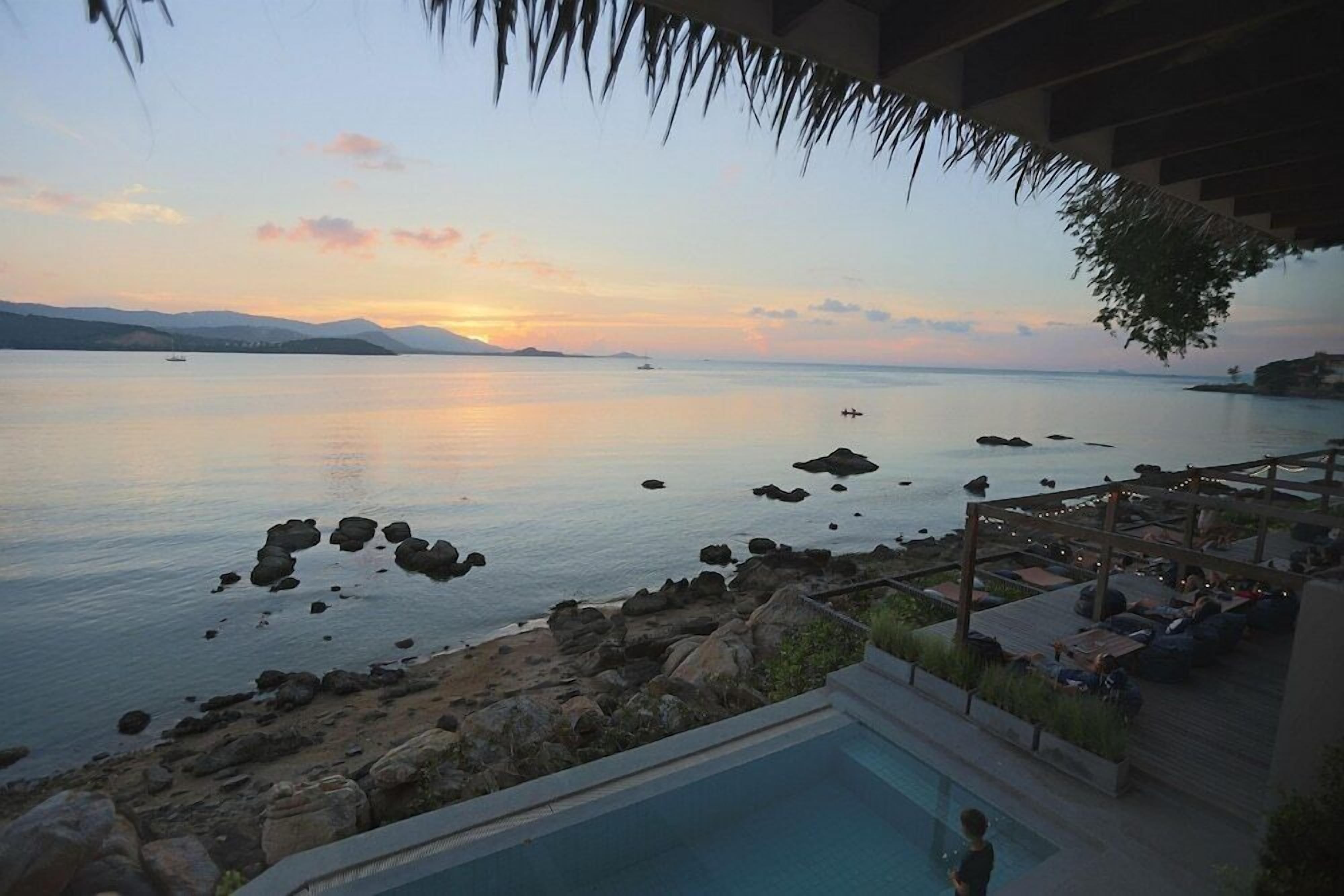 Zona de piscina con vista al mar y montañas distantes al atardecer.