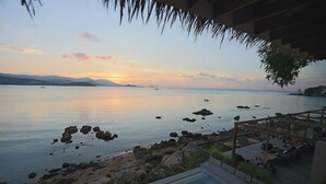 Zona de piscina con vista al mar y montañas distantes al atardecer.