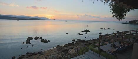 A pool area with a view of the sea and distant mountains during sunset.