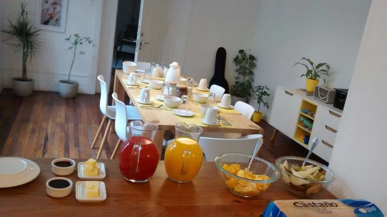 Un comedor con una mesa de madera lista para el desayuno, con platos, tazones y una jarra de jugo de naranja.