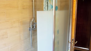 A glass-enclosed shower with a showerhead and control panel, a tiled floor, and a wooden door leading to another room. - Ca' Concordia Venice (Mestre)