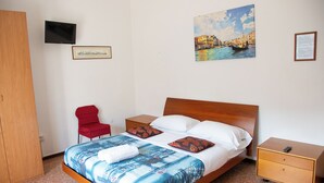 A hotel room with a bed, a TV, a red chair, a wooden wardrobe, and a painting of a cityscape. - Ca' Concordia Venice (Mestre)