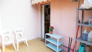 Una habitación pequeña con una puerta blanca, una silla blanca, un estante azul y un estante metálico con productos de limpieza.