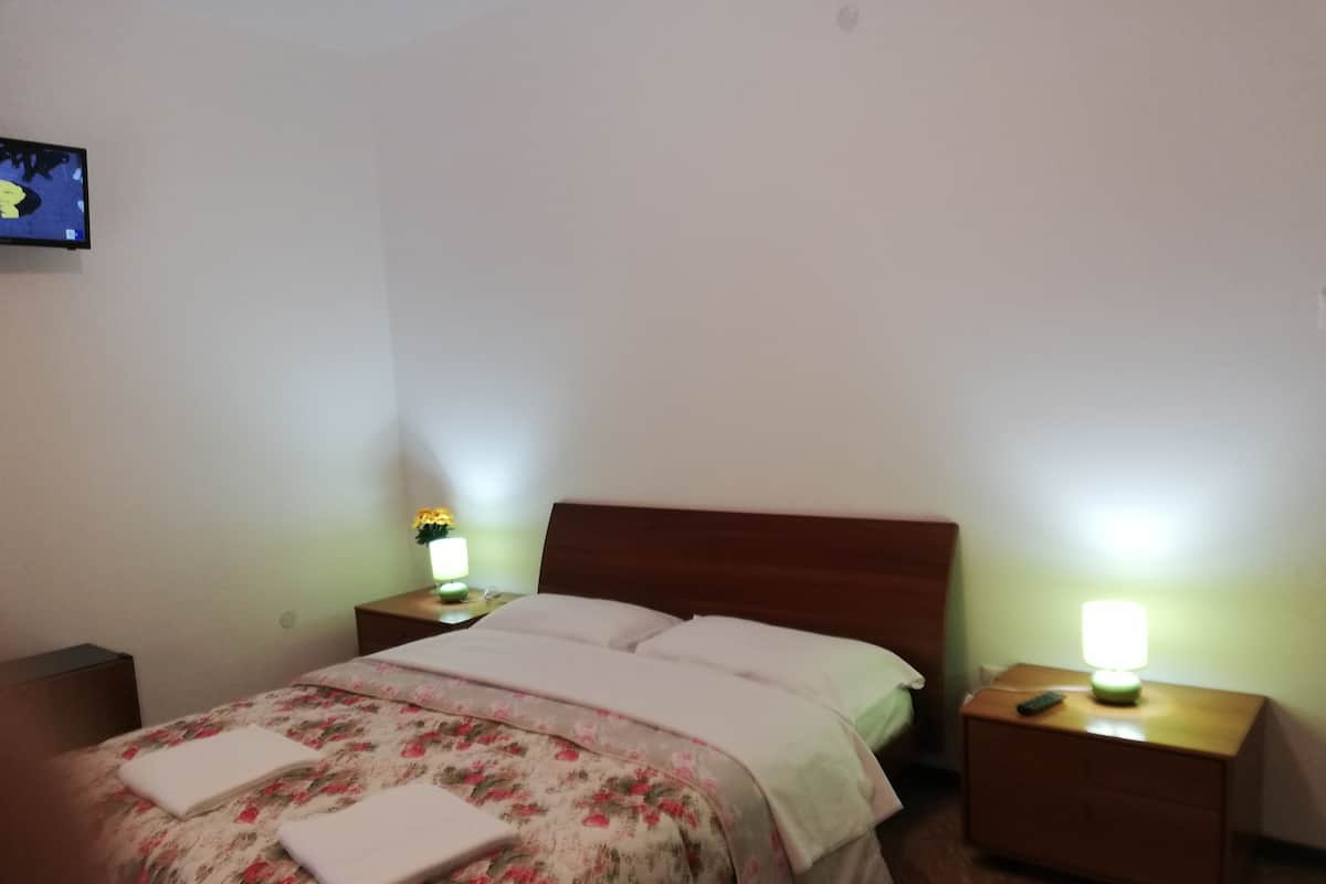 A hotel room with a bed, two bedside tables with lamps, a TV on the wall, and a floral bedspread.