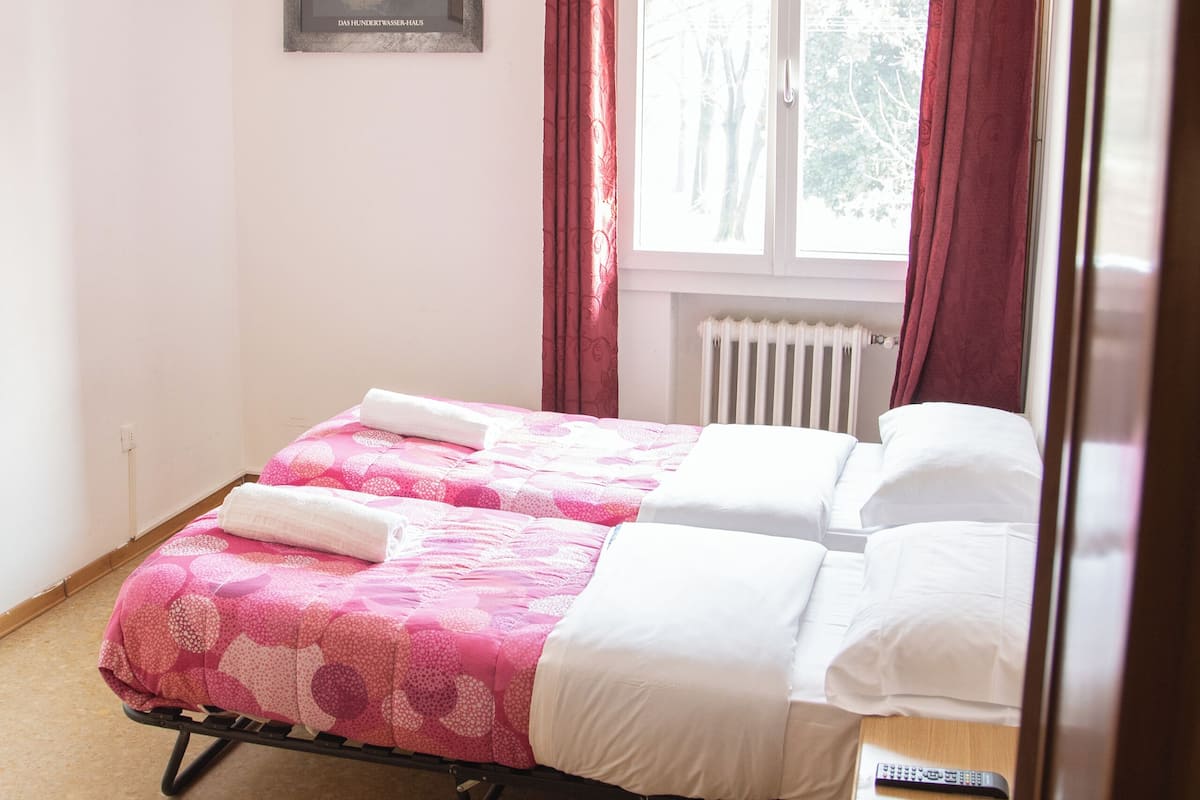 A bedroom with a bed, a nightstand, a framed picture on the wall, and a window with curtains.