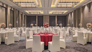 A banquet hall with round tables set for dining, white chairs, and floral centerpieces.