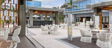 Un patio al aire libre con mobiliario de mimbre, un bar y vistas de un edificio moderno.