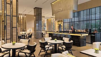 A modern bar area with a bartender, round tables, and bar stools.