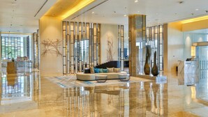 A modern lobby with a reflective marble floor, a seating area with a sofa and coffee table, and a reception desk.