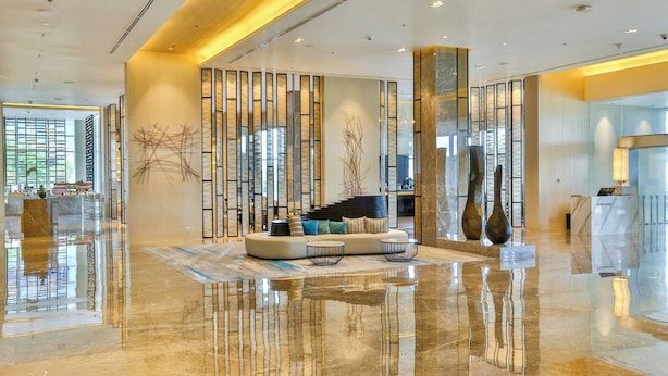 Um lobby moderno com piso de mármore refletivo, área de estar com sofá e mesa de centro, e um balcão de recepção.