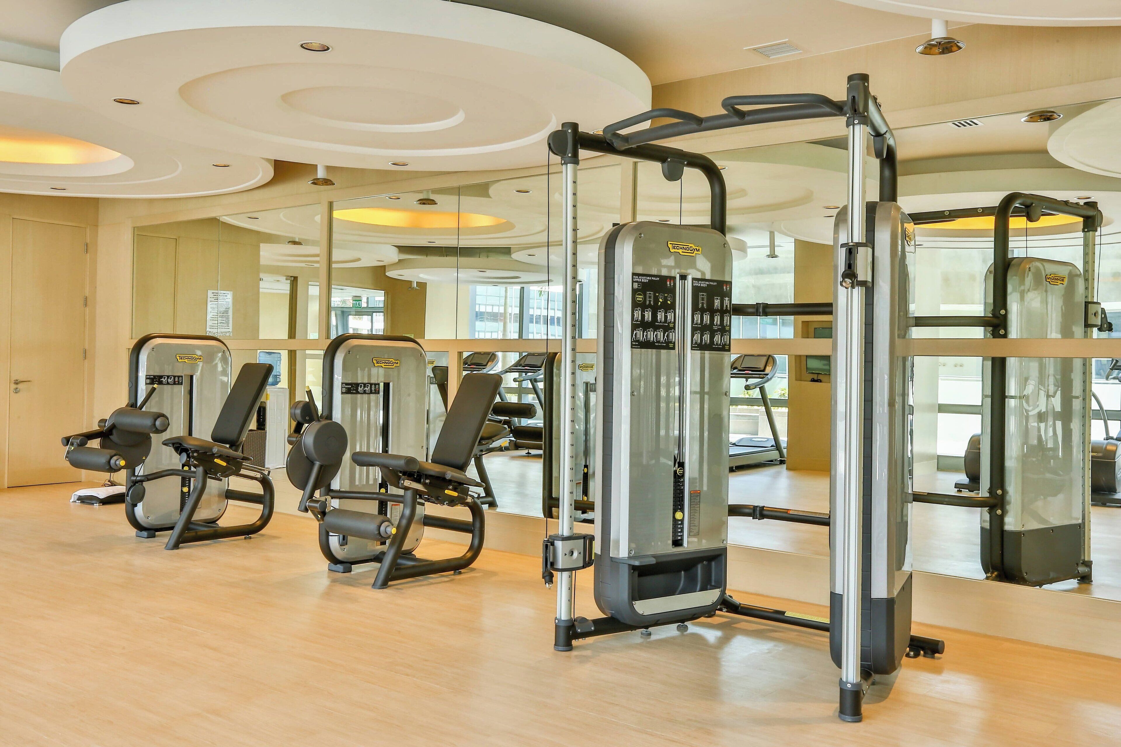 A gym with exercise machines, wooden flooring, and a large mirror.