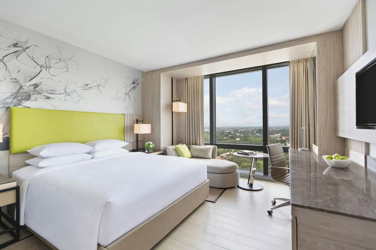 A modern hotel room with a large bed, a seating area with a view, and a dining table.