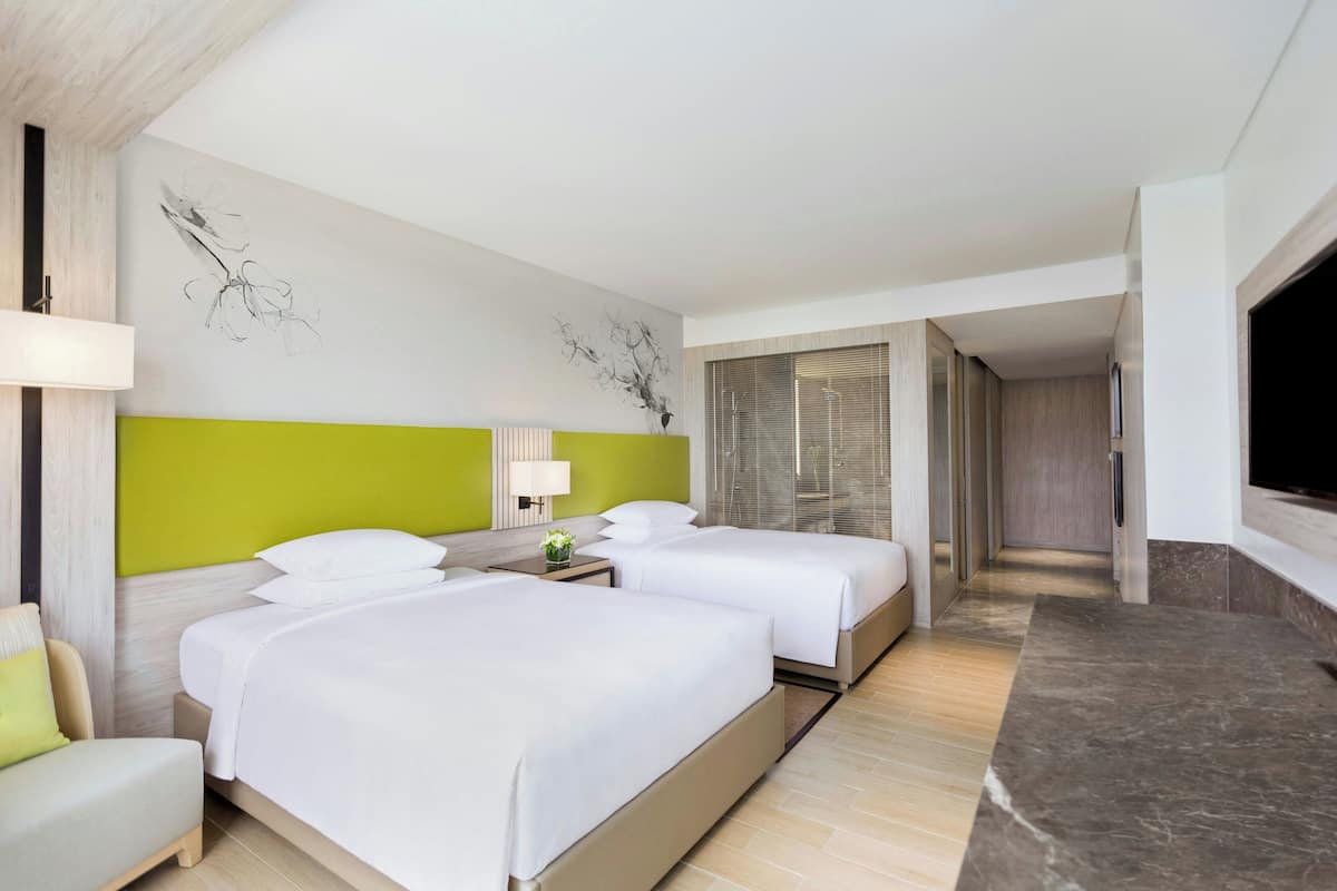 A hotel room with two beds, a TV, a desk, and a bathroom.