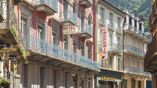 Un hôtel doté de balcons, une enseigne indiquant « HÔTEL Christian », et un commerce appelé « CRÊPERIE » de l’autre côté de la rue.