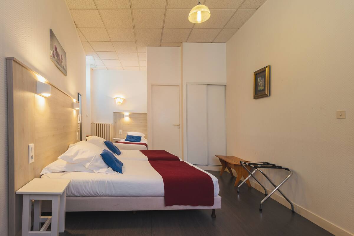 A hotel room with two beds, a wooden bench, a desk, and a chair.